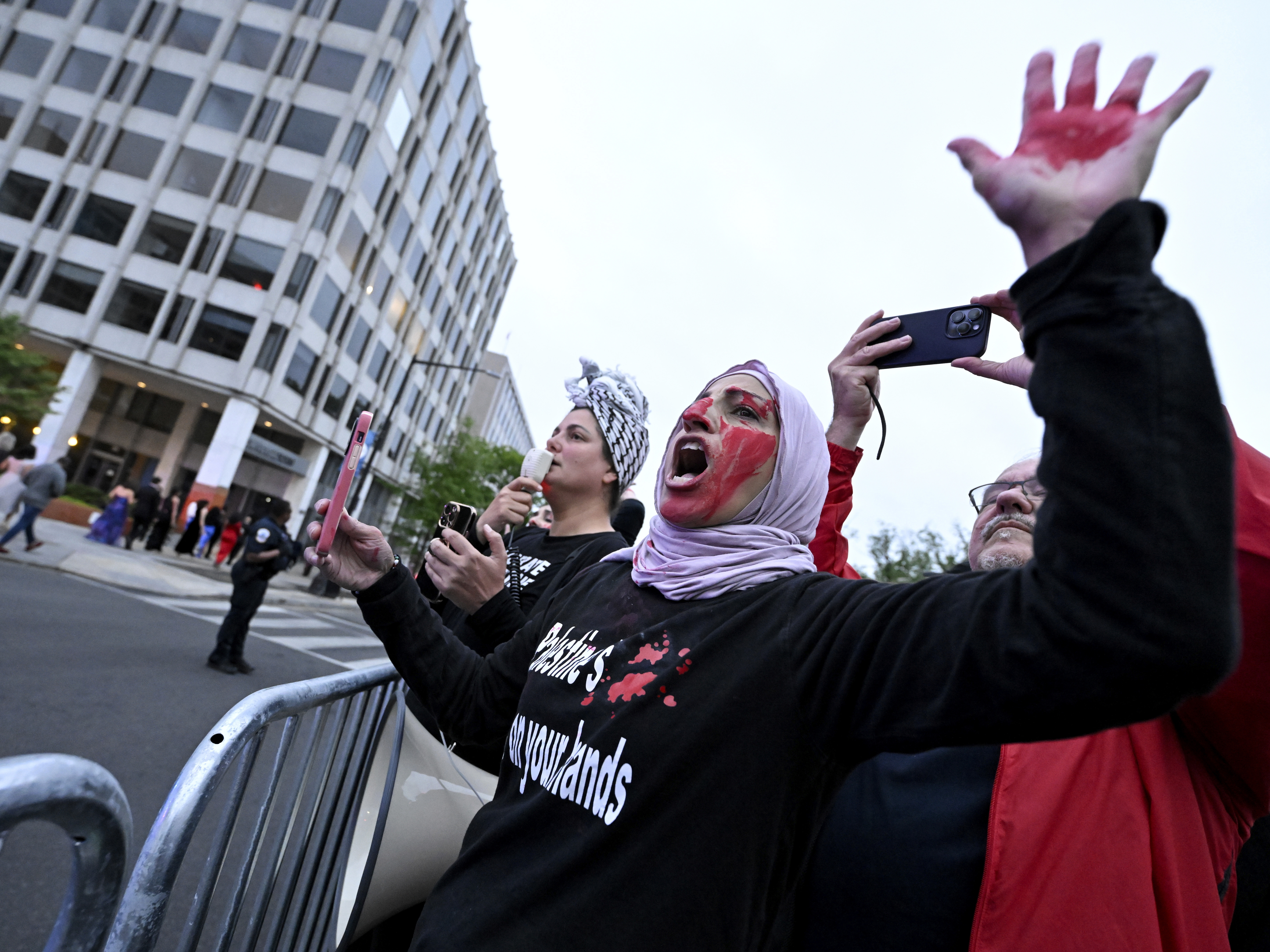 A demonstrator with red paint on their hand and face is seen behind a police barricade during a pro-Palestinian protest over the Israel-Hamas war at the White House Correspondents